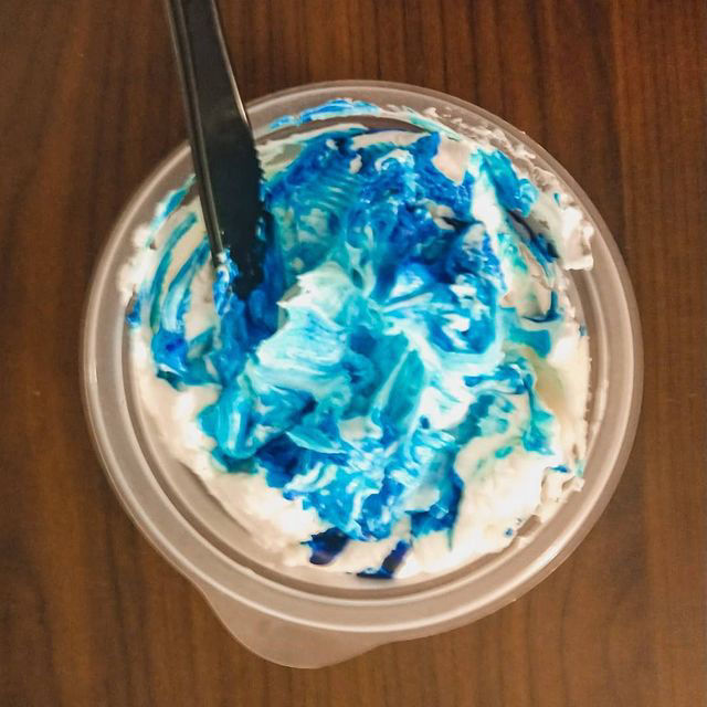 A bowl of partially mixed icing and food coloring.