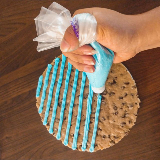 A hand piping frosting onto a round cookie cake.